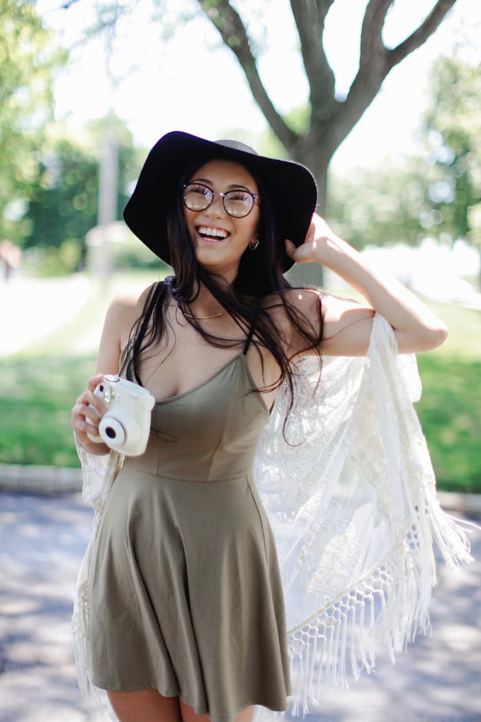 Cheerful woman in a boho dress with a camera enjoying a sunny day outdoors.